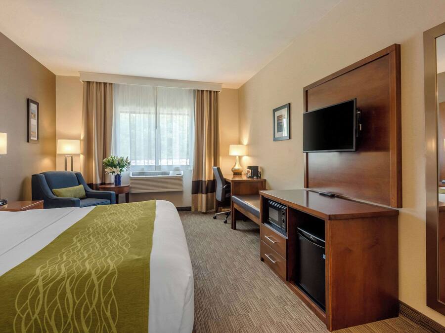 A hotel room with a large bed, a desk, a television, and a mirror.