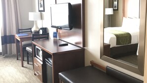 Una habitación de hotel con escritorio, televisión, espejo, cama y ventana con cortinas.