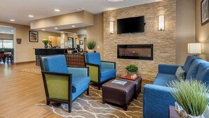 Un vestíbulo de hotel con mostrador de recepción, zona de estar con sofás y sillones, un televisor de pantalla plana montado en una pared de piedra y una chimenea.