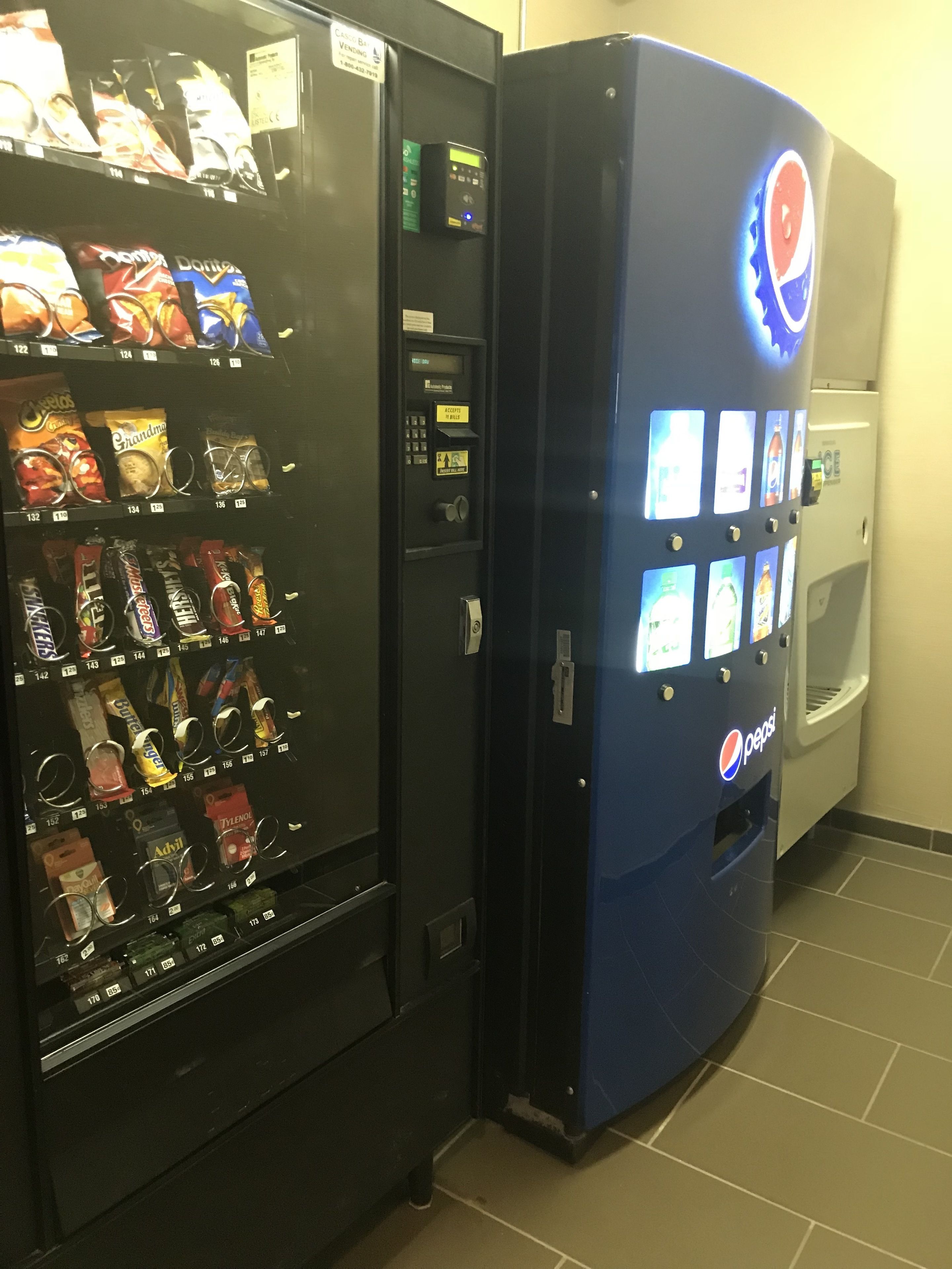En automattank med en Pepsi-logotyp och en digital display, placerad bredvid en annan automattank som säljer olika typer av snacks.