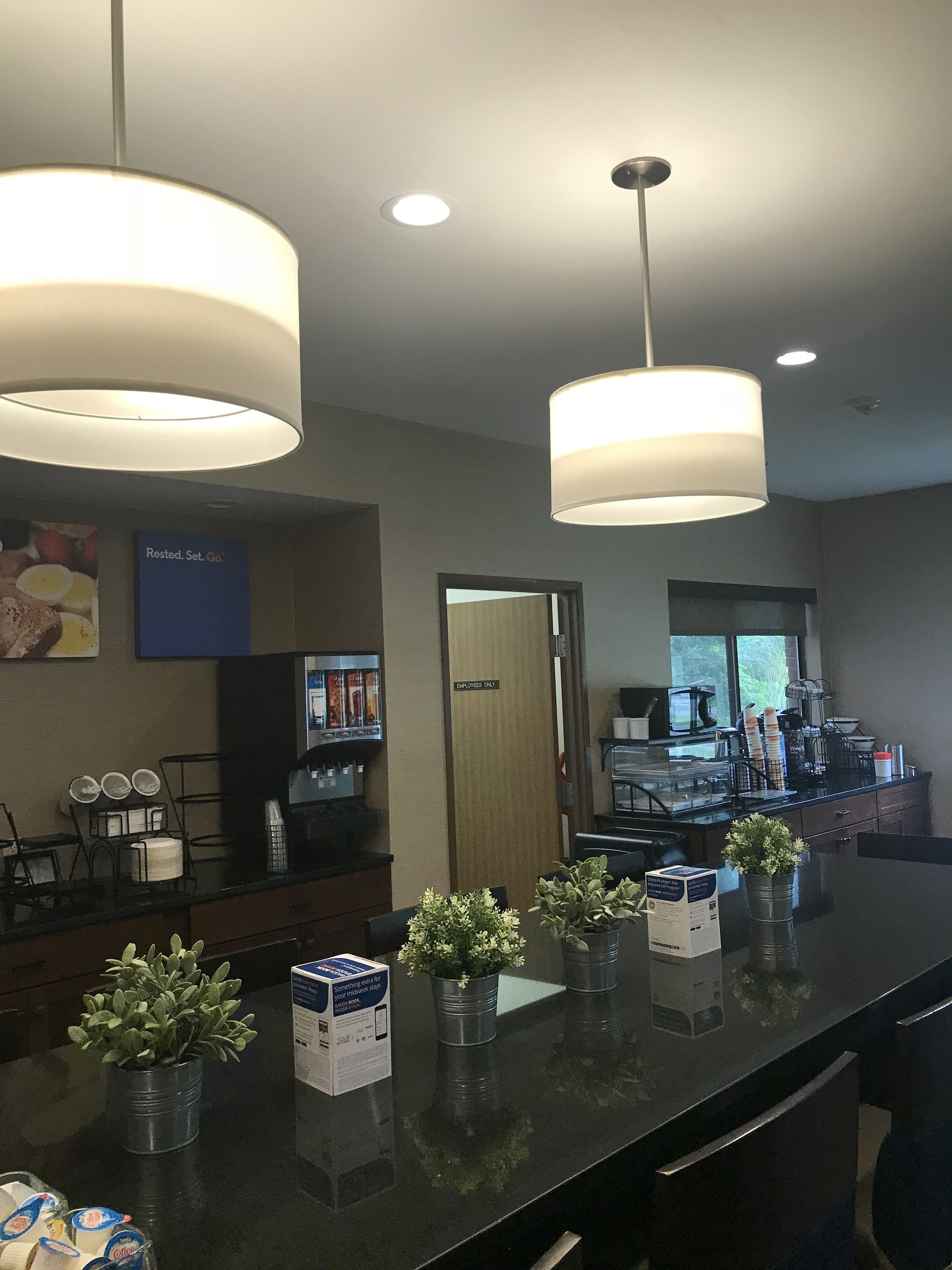 A hotel lobby with a reception desk, two pendant lights, a coffee station, and a sign indicating it's an employee-only area.
