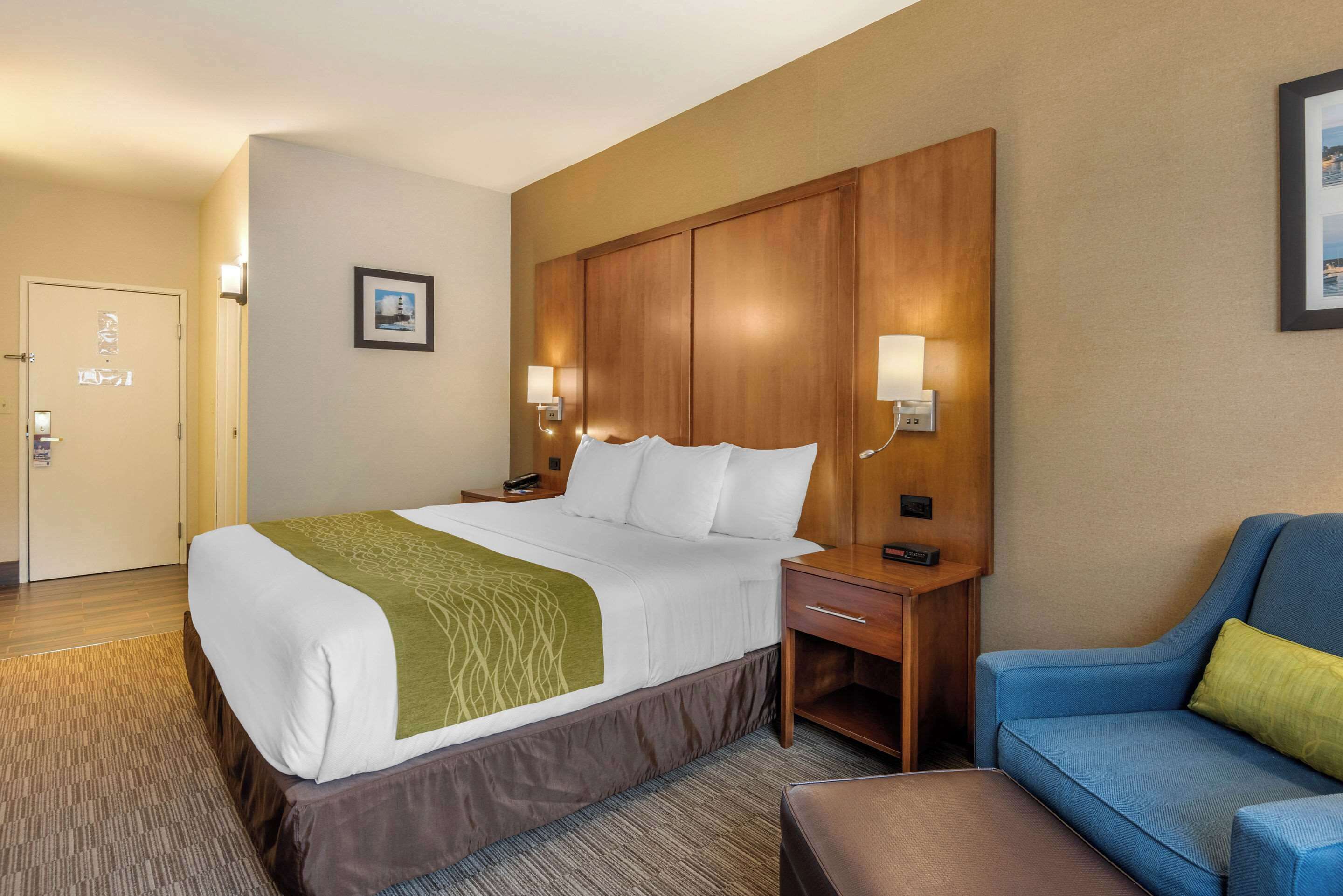 Ein Hotelzimmer mit einem großen Bett, einem Holz-Kopfteil, zwei Nachttischen mit Lampen, einem blauen Sofa und einem kleinen Tisch ebenfalls mit einer Lampe.