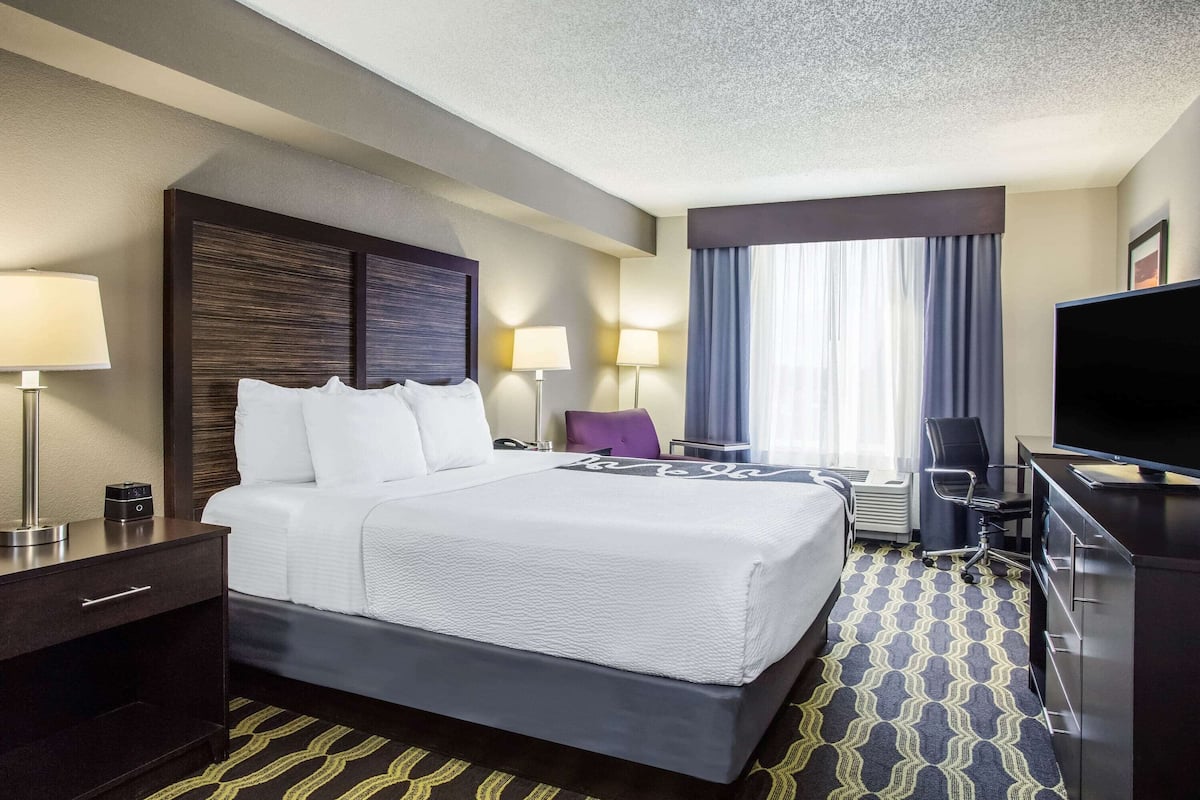 A hotel room with a large bed, bedside tables, a desk, a chair, and a television.