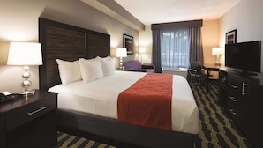 Una habitación de hotel con una cama grande, dos mesitas de noche con lámparas, un escritorio con silla, un televisor y una ventana con cortinas.