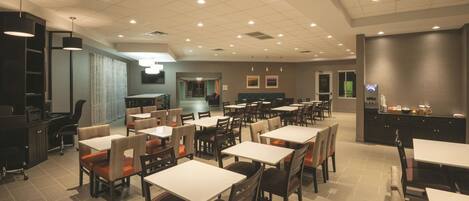 A spacious dining area with multiple tables and chairs, a kitchen area, and a reception desk.