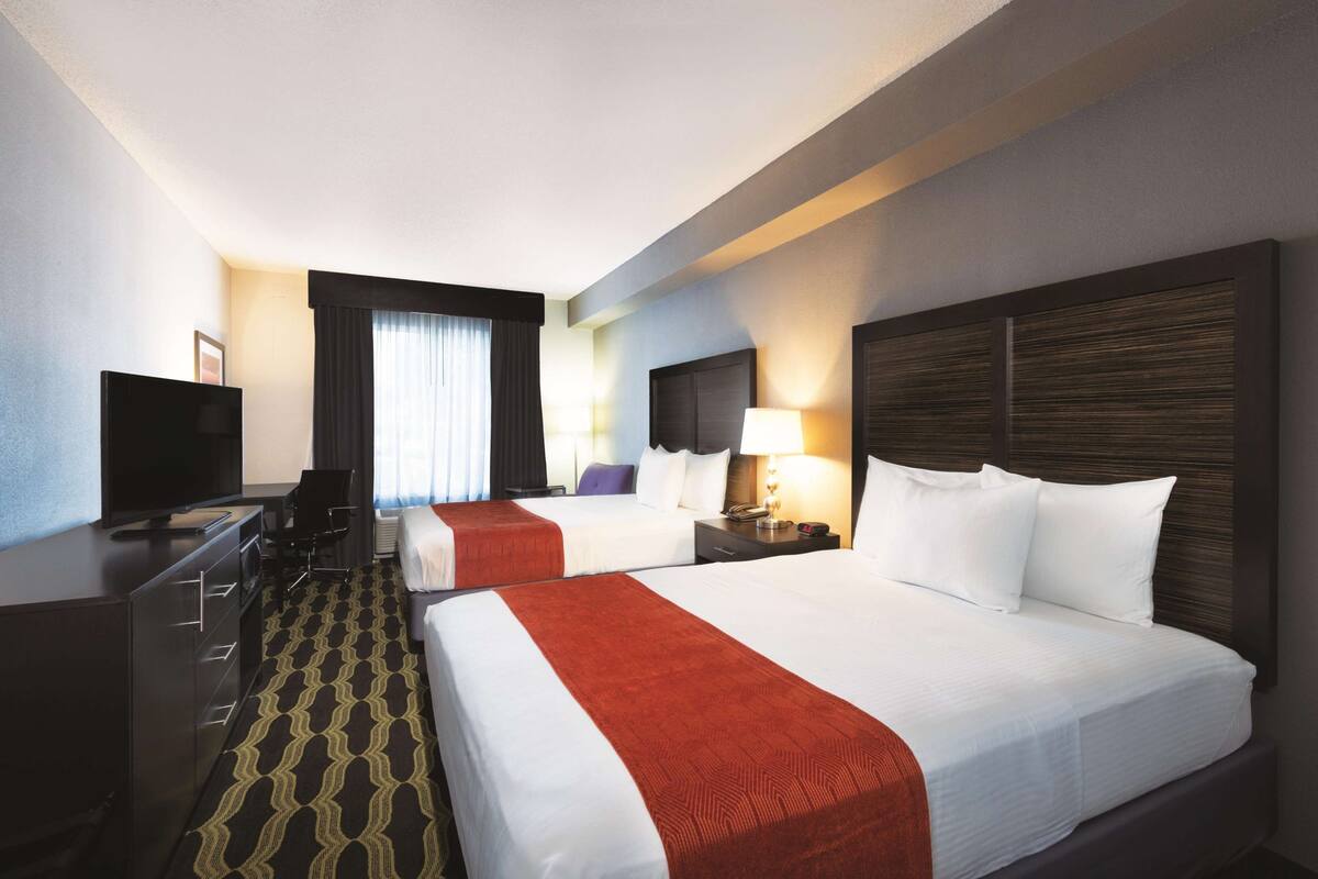 A hotel room with two beds, a desk with a TV, and a chair.