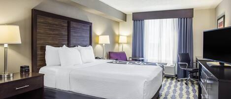 Quarto de hotel com cama, luminárias de cabeceira, uma escrivaninha com televisão e uma cadeira.