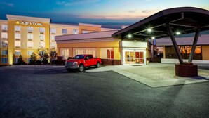 Entrada de hotel con una camioneta roja estacionada frente, un corredor cubierto y un edificio con un letrero que dice "LA QUINTA JIMNA SUITES".