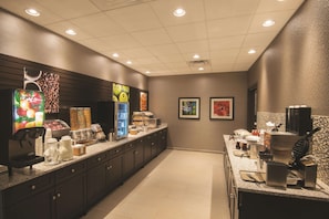 A modern kitchen area with a coffee machine, a juice dispenser, and a waffle maker.