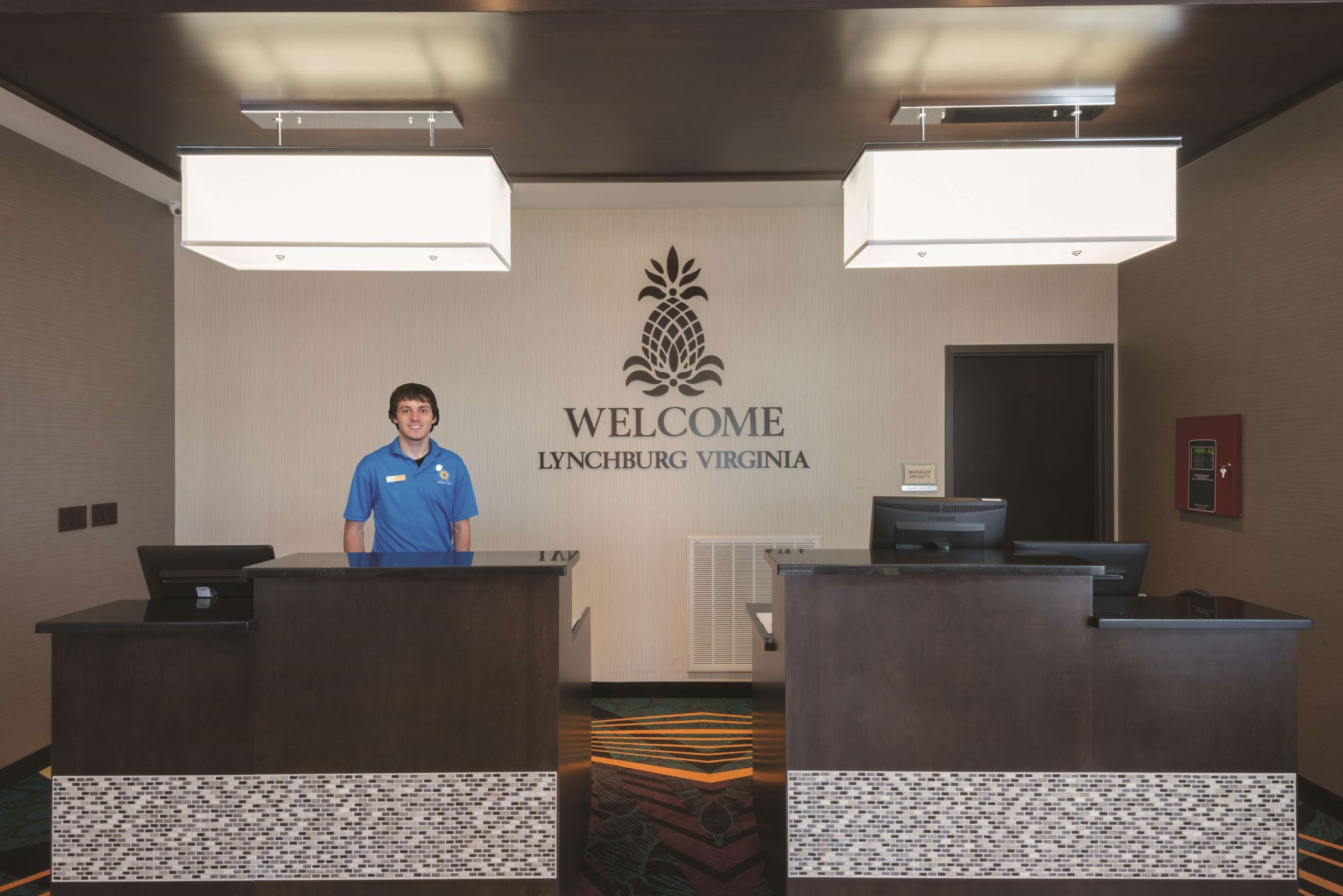 En receptionsdisk med en skylt som lyder ”VÄLKOMMEN TILL LYNCHBURG, VIRGINIA”, två receptionspersonal och en modern design med ett mönstrat golv.