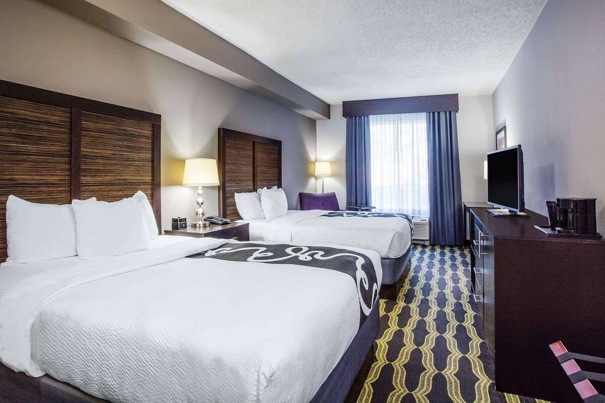 A hotel room with two beds, a desk, a TV, and a window with curtains.