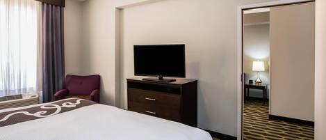 Habitación de hotel con cama, televisor en una cómoda, una silla y una puerta que da a otra habitación.
