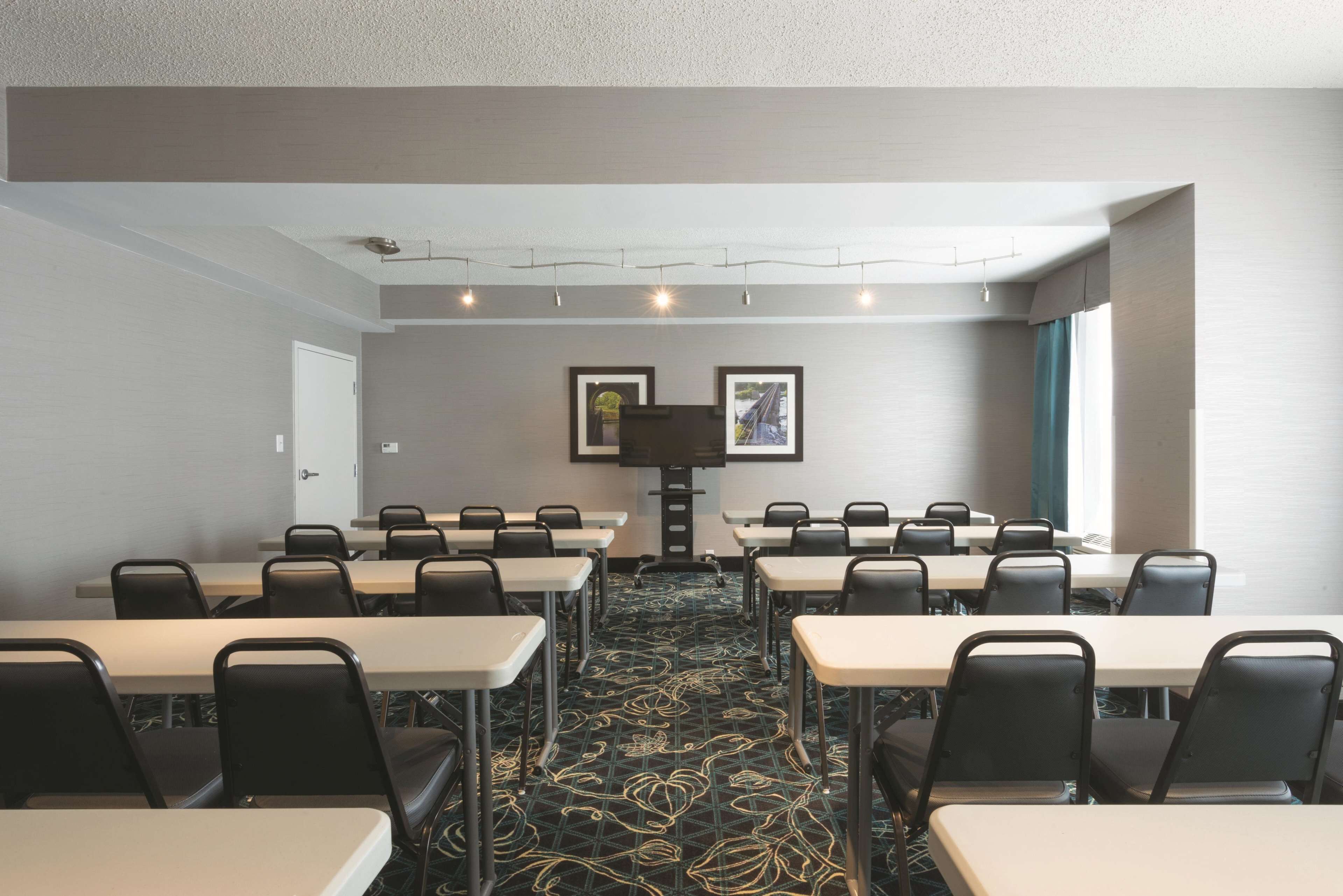 A conference room with tables and chairs, a projector screen, and framed pictures on the wall.