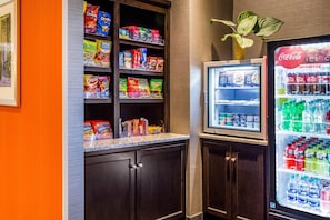 A vending machine with snacks and beverages, a refrigerator with drinks, and a potted plant.
