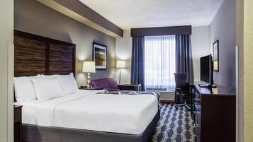 Habitación de hotel con una cama grande, un escritorio con silla, un televisor y una ventana con cortinas.