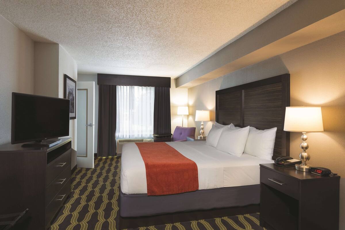 A hotel room with a bed, a television, a desk with a lamp, and a nightstand with a lamp.