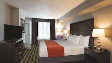 A hotel room with a bed, a television, a desk with a lamp, and a nightstand with a lamp.