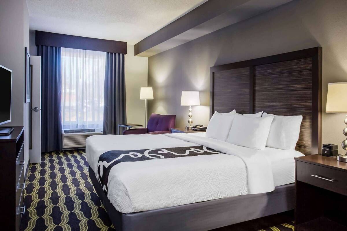 A hotel room with a large bed, a desk, a chair, a TV, and a window with curtains.