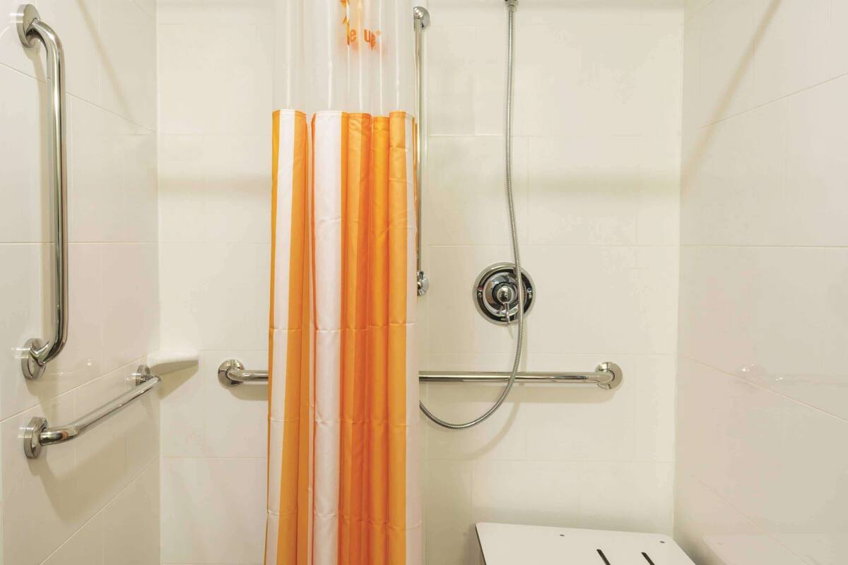 A shower area with a handrail, a showerhead, and a control panel.
