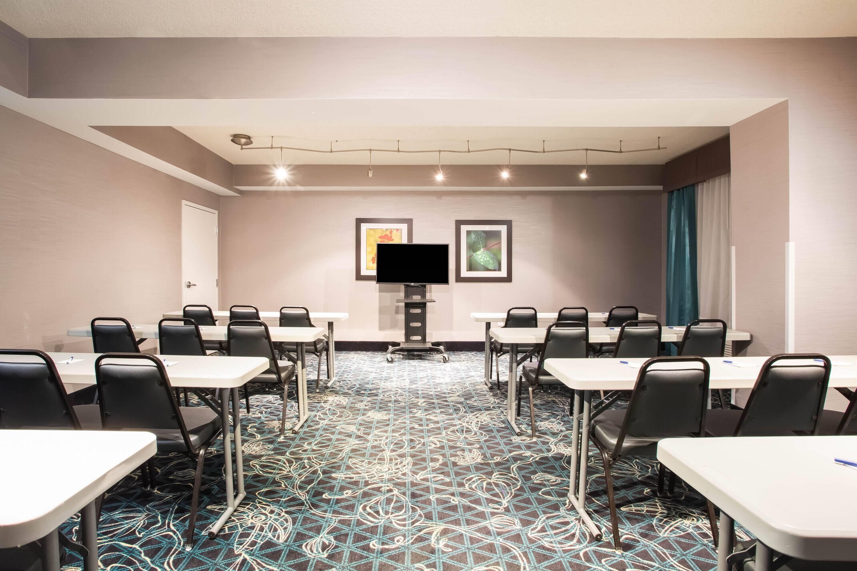 Une salle de conférence équipée de tables et de chaises, d’un téléviseur à écran plat et d’œuvres d’art encadrées accrochées au mur.