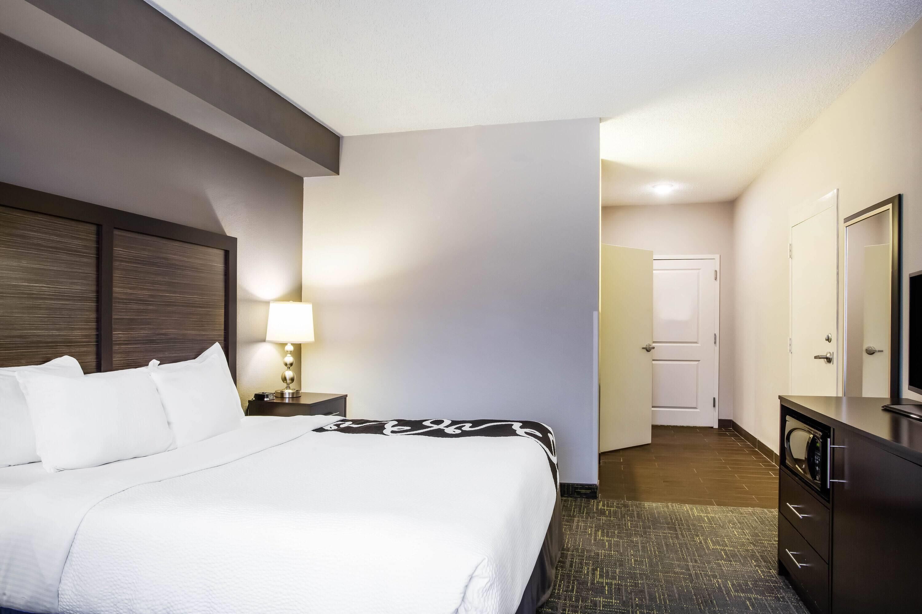 A hotel room with a bed, bedside lamp, dresser, and a door leading to a bathroom.