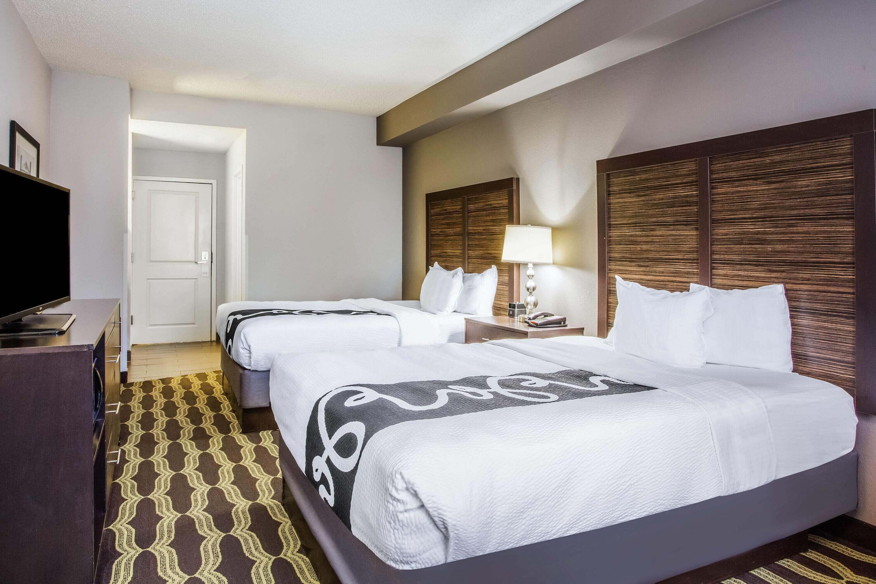 A hotel room with two beds, a TV, a desk, and a patterned rug.