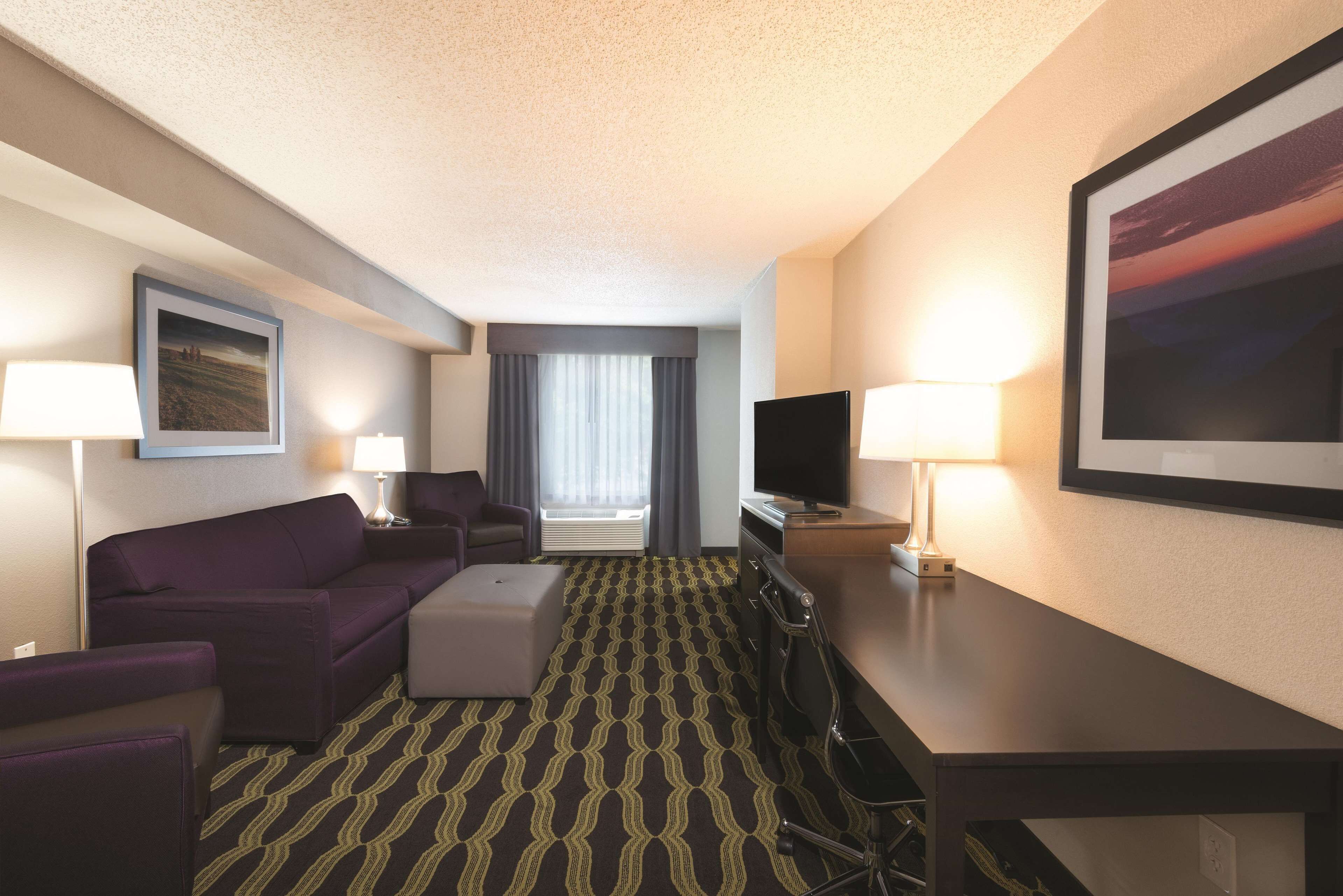 A hotel room with a sofa, a TV, a desk, and a patterned carpet.