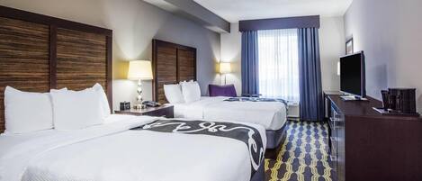 A hotel room with two beds, a desk, a television, and a window with curtains.