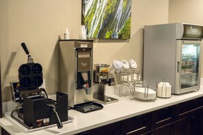 A breakfast bar with a waffle maker, a coffee machine, a refrigerator, and a painting on the wall. - Sleep Inn & Suites Omaha Airport (Omaha)