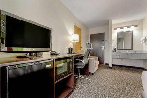 Habitación de hotel con televisión de pantalla plana, escritorio con lámpara, silla, microondas y espejo grande.