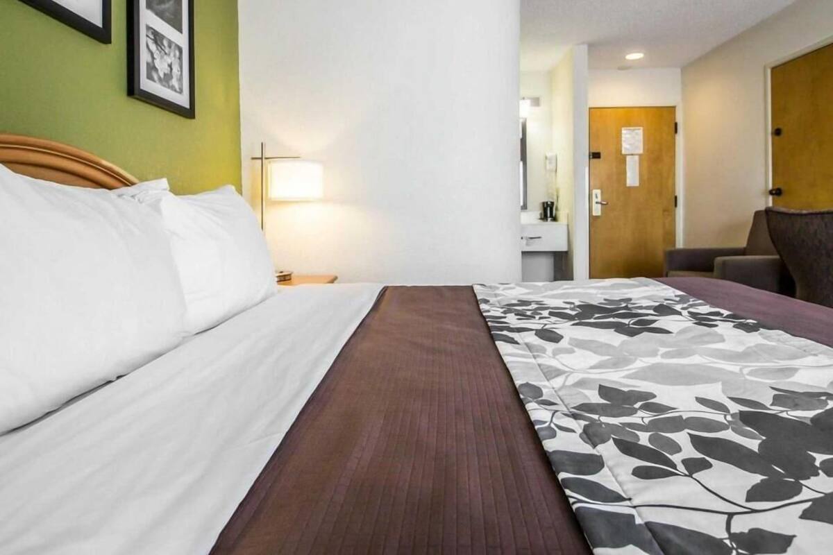 A hotel room with a bed, a nightstand, a lamp, a chair, and a door.