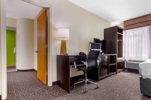 Habitación de hotel con escritorio, silla, lámpara, televisión, armario y cama.