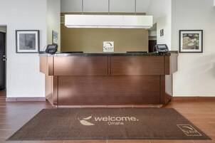 Un comptoir d’accueil avec une enseigne « Sleep Inn & Suites », un tapis « Bienvenue à Omaha » et deux terminaux de paiement « Choice ».