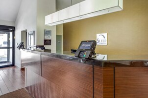 Un mostrador de recepción con un terminal de pago digital, un letrero de 'SLEEP INN & SUITES' y una ventana con vistas al exterior.