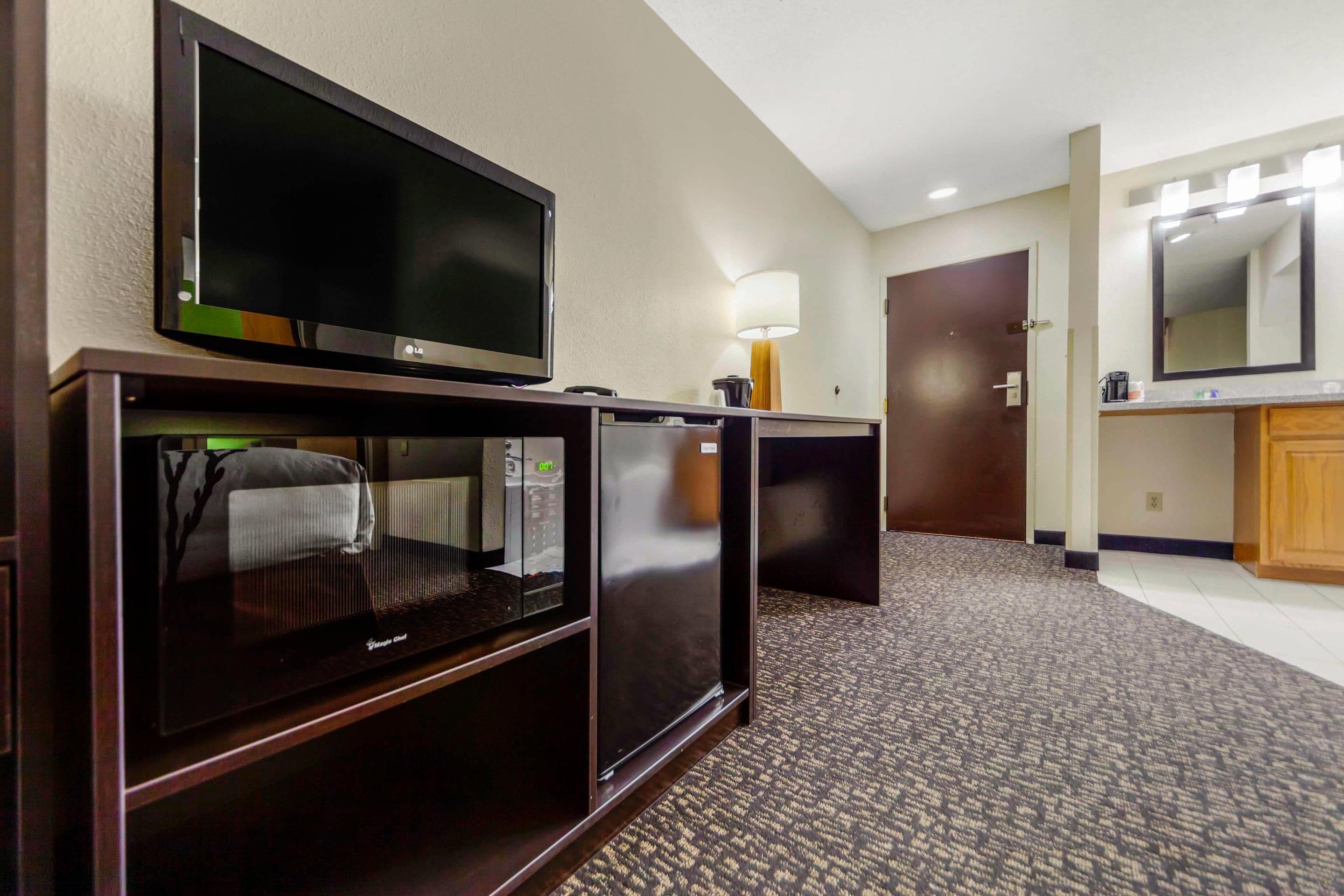 A hotel room with a flat-screen TV, a minibar, a lamp, and a mirror.