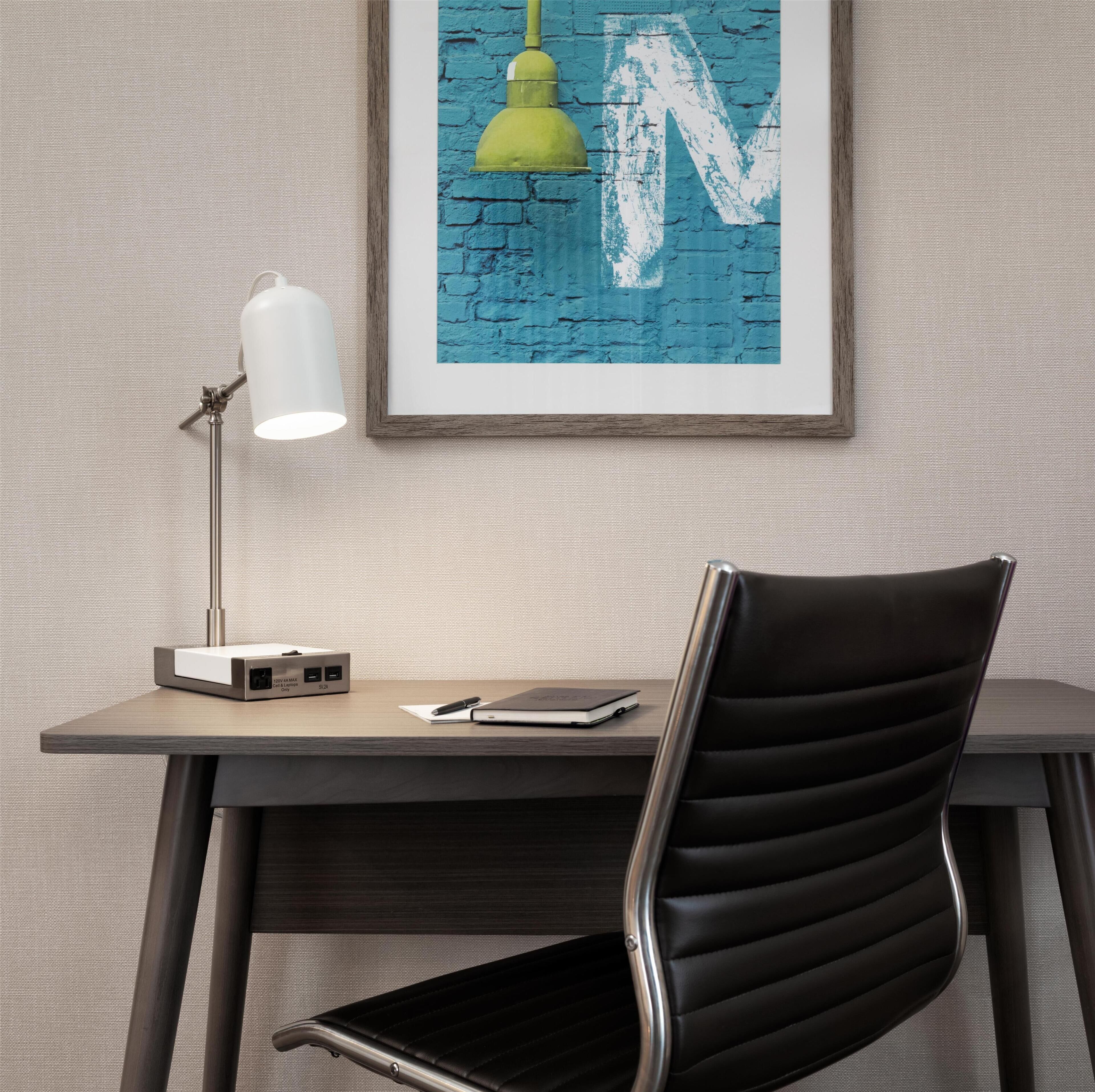 Un espacio de trabajo moderno con escritorio, lámpara, silla y una obra de arte enmarcada en la pared.