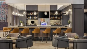 Un espace bar moderne doté d’un long comptoir, de nombreux tabourets et d’une variété de bouteilles et de verres exposés sur des étagères.
