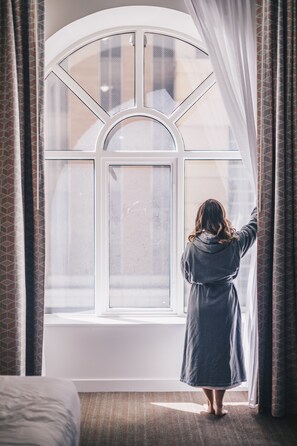 A person standing by a large arched window with curtains, in a room with a bed and patterned curtains. - Hyatt Centric Downtown Minneapolis (Minneapolis)