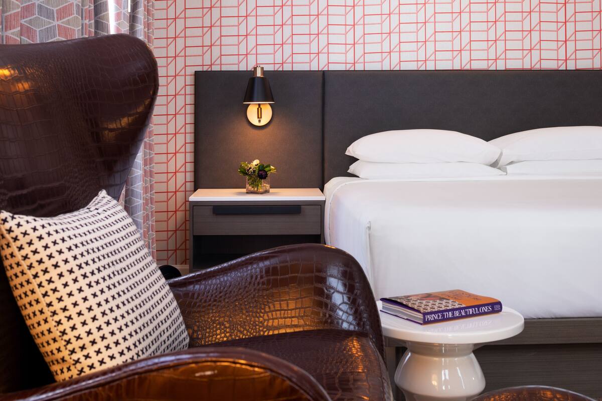 Une chambre d’hôtel avec un lit, une table de chevet avec une lampe, une chaise et une petite table sur laquelle se trouve un livre.