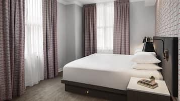 A modern hotel room with a large bed, a bedside table with a lamp, and patterned curtains.