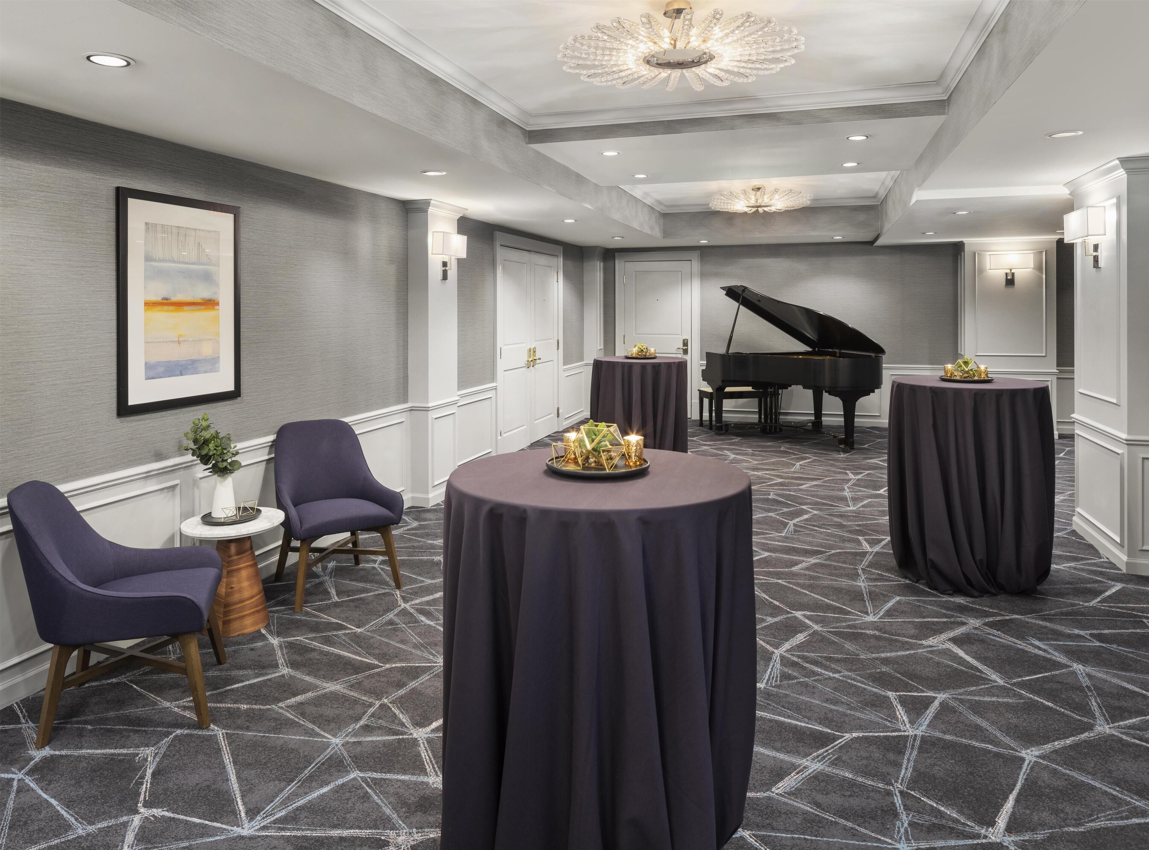 A hotel room with a grand piano, round tables, and modern decor.