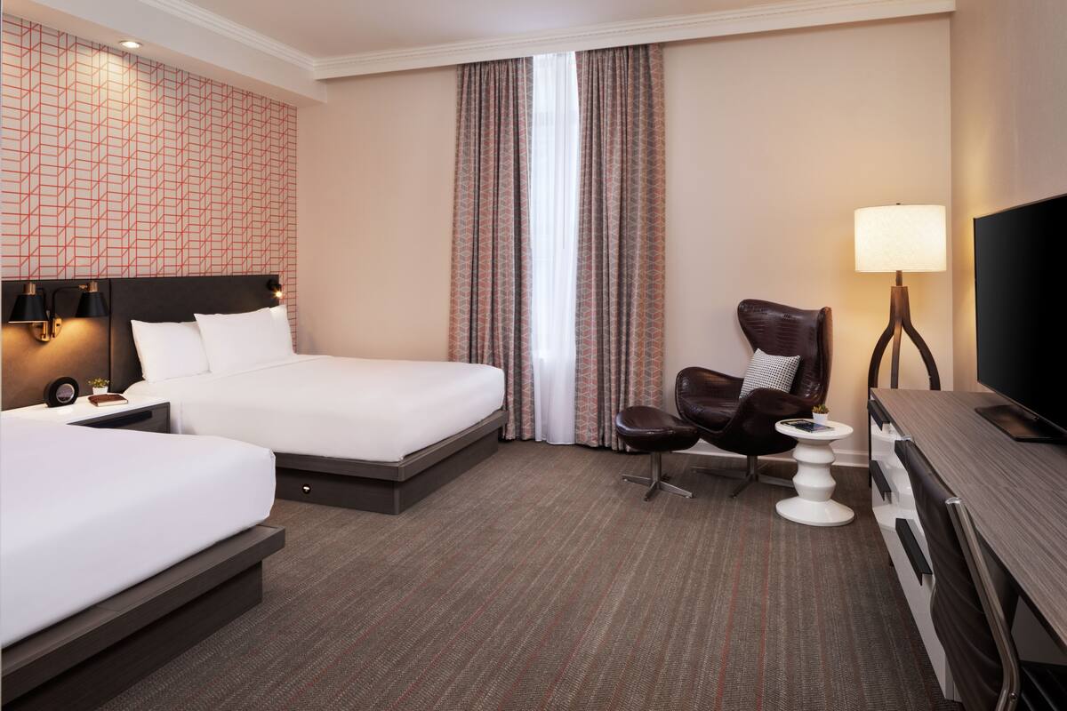 Une chambre d’hôtel avec deux lits, un bureau, une chaise, une télévision et une lampe.