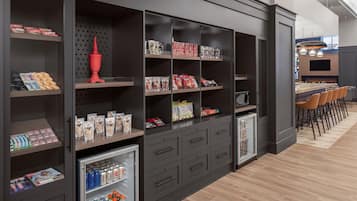 Un espace bar moderne doté d’un long comptoir et de nombreux tabourets, entouré d’éléments de rangement sombres où sont exposés divers en-cas et boissons.