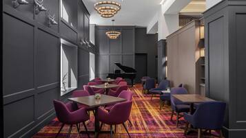 A modern hotel lobby with a grand piano, plush seating, and decorative wall mounts.