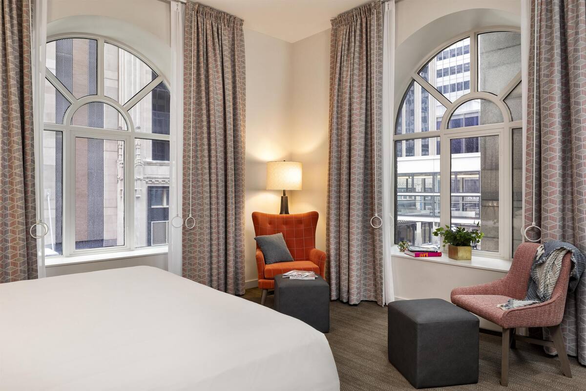 Une chambre d’hôtel avec un grand lit, deux fauteuils, une petite table et une lampe.