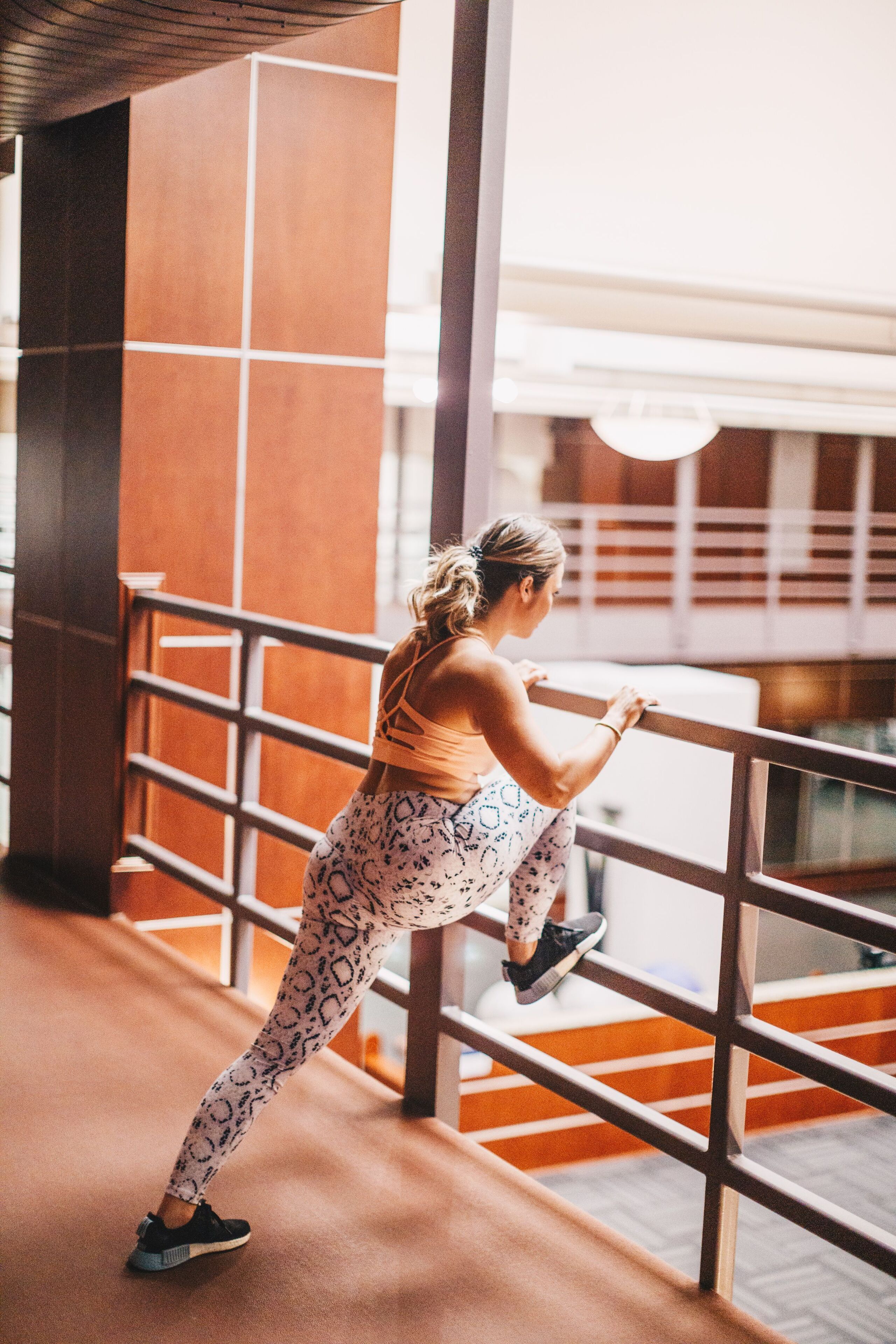 A person exercising on a balcony with a railing, a view of the building's interior, and a staircase.