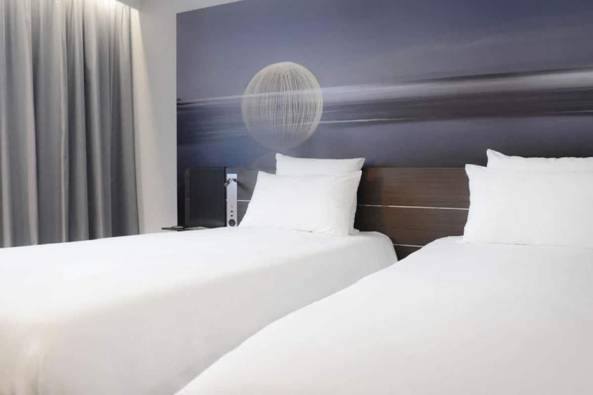 A hotel room with two beds, a large window with curtains, and a wall mural.