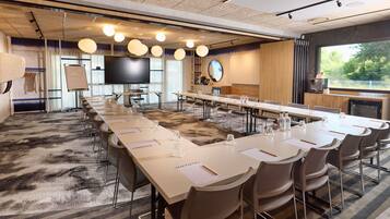 Une salle de conférence avec une longue table, des chaises, un téléviseur et une grande fenêtre.
