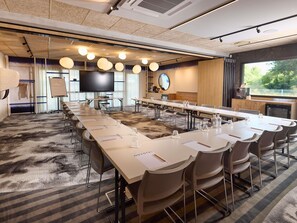 Une salle de conférence avec une longue table, des chaises, un téléviseur et une grande fenêtre.