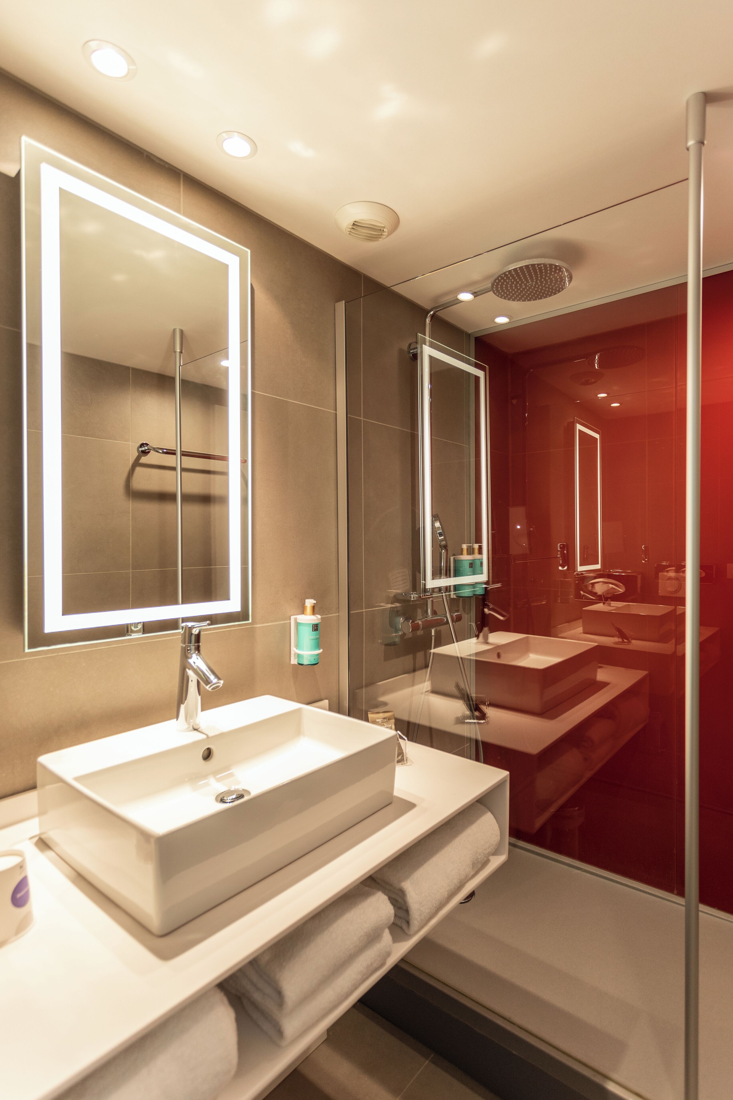 A modern bathroom with a large mirror, two sinks, and a glass shower enclosure.